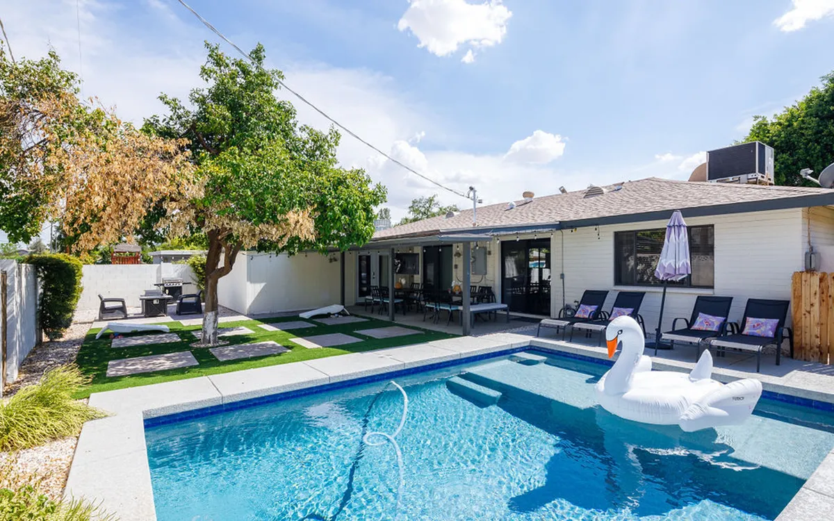 The hero image showcases a sparkling swimming pool with a whimsical swan float, surrounded by inviting lounge chairs and a shady tree. The spacious patio area hints at outdoor dining and barbecues, all set against the relaxed vibe of an Arizona sunset.