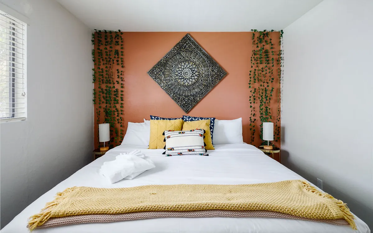 A comfortable and serene bedroom featuring a plush bed topped with colorful pillows and a decorative throw blanket. Large wall art adds character, and soft natural light creates a tranquil setting for relaxation or quiet reading.