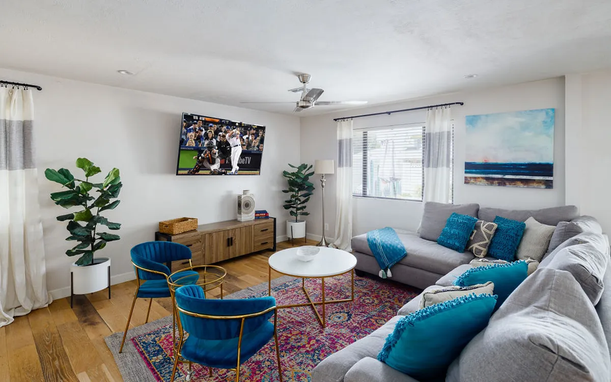 A spacious living room featuring a large sectional sofa, an inviting coffee table, a smart television, decorative plants, and stylish artwork. The arrangement encourages gatherings and socializing, and the décor is influenced by Art Deco elements, with clean lines and rich textures.