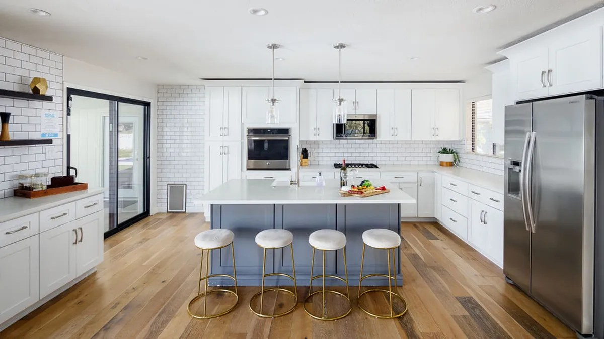A bright, spacious kitchen featuring a large island with bar stools, gleaming stainless steel appliances, white cabinetry, and a classic subway tile backsplash. The island is perfect for prepping meals or gathering with friends and family, while the appliances and cabinetry showcase the kitchen's high-end, fully stocked feel.